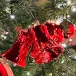 Glasgl&ouml;ckchen, rot, gl&auml;nzend, h&auml;ngend im gr&uuml;nen Weihnachtsbaum, in dem unz&auml;hlige Lichtlein wie Sterne strahlen.